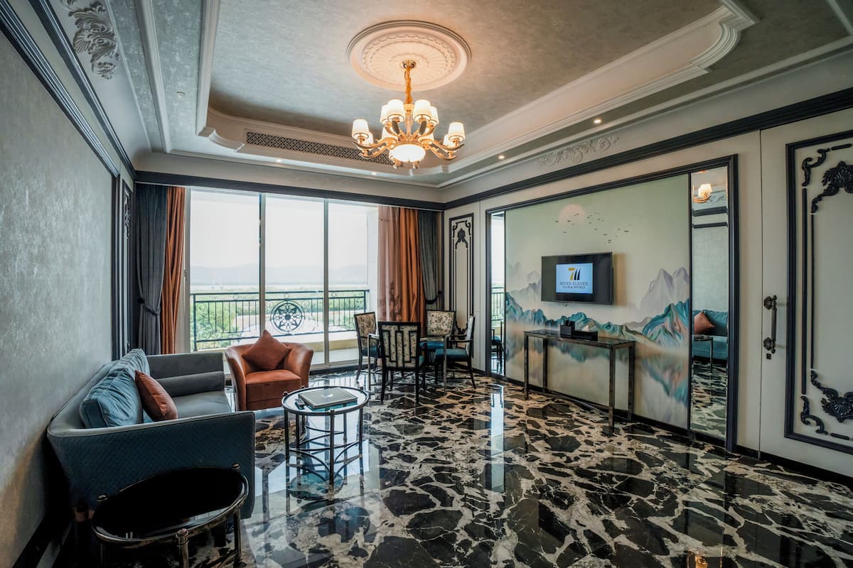 A hotel lobby with a chandelier, seating area, large windows, and a television.
