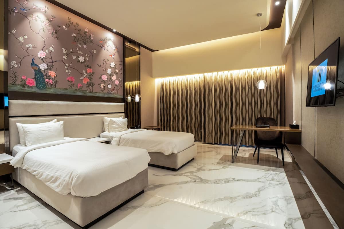 A hotel room with two beds, a desk, a chair, a TV, and a decorative wall with floral art.