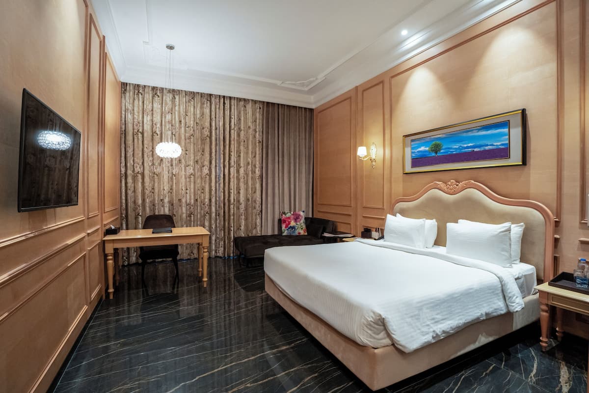 A hotel room with a large bed, a desk, a chair, a television, and a painting on the wall.