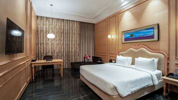 Habitación de hotel con una cama grande, un escritorio, una silla, un televisor y un cuadro en la pared.