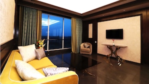 A modern hotel room with a yellow sofa, a small armchair, a flat-screen TV, and a large window with curtains. - Seven Eleven Club (Mumbai)