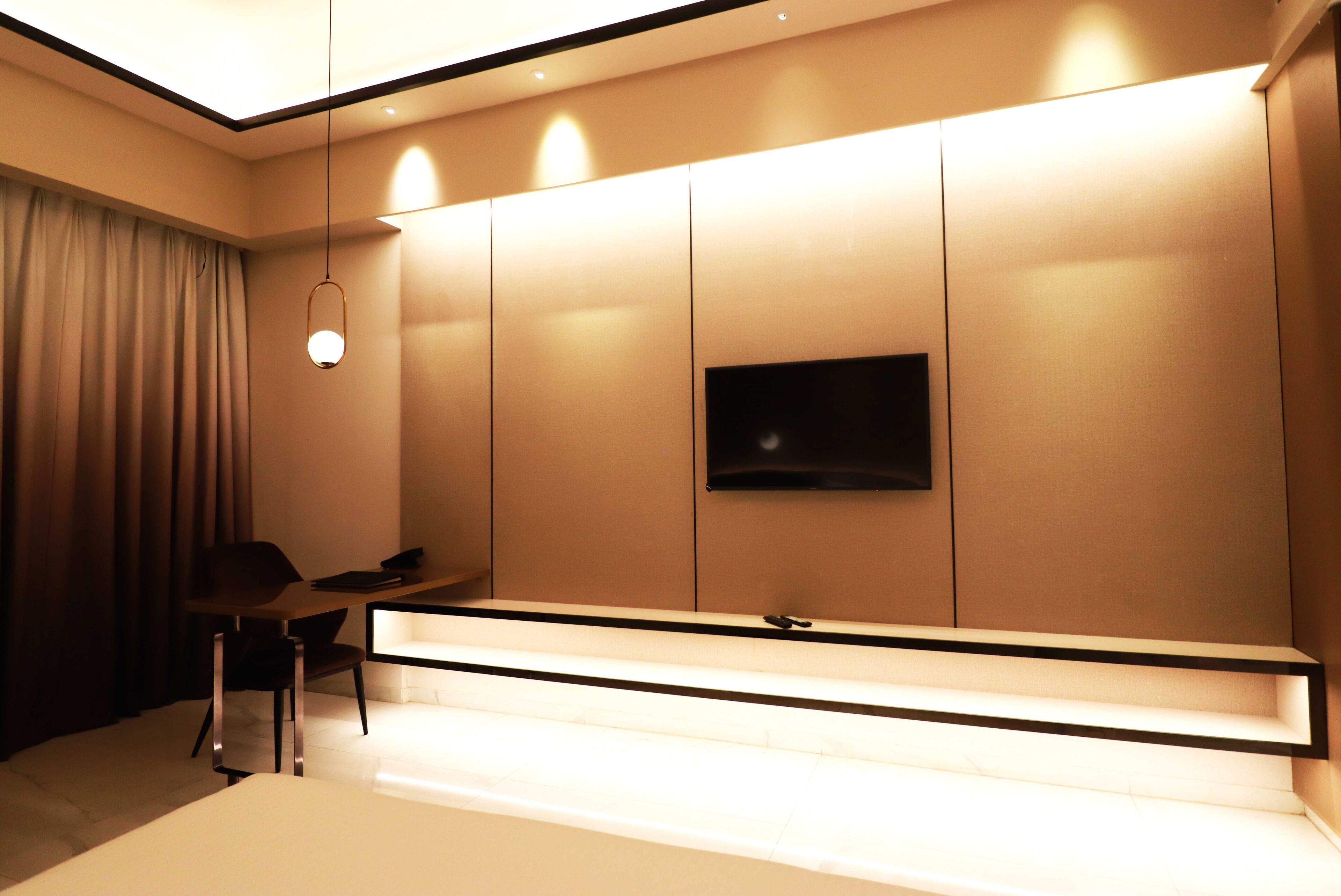 Habitación de hotel moderna con televisión de pantalla plana montada en la pared, un escritorio con silla y un amplio ventanal con cortinas.