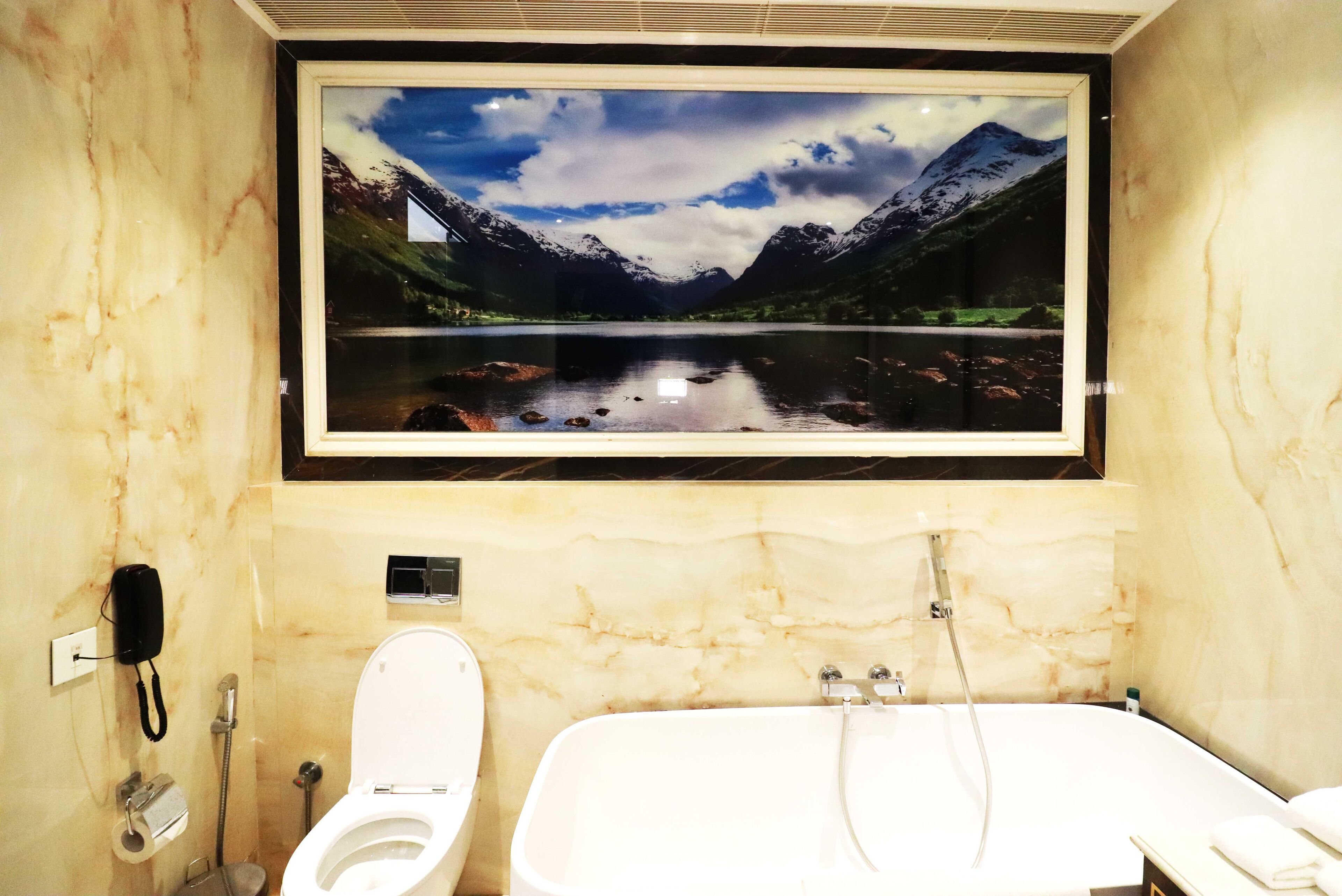 A bathroom with a large framed picture of a mountain landscape, a toilet, and a bathtub.