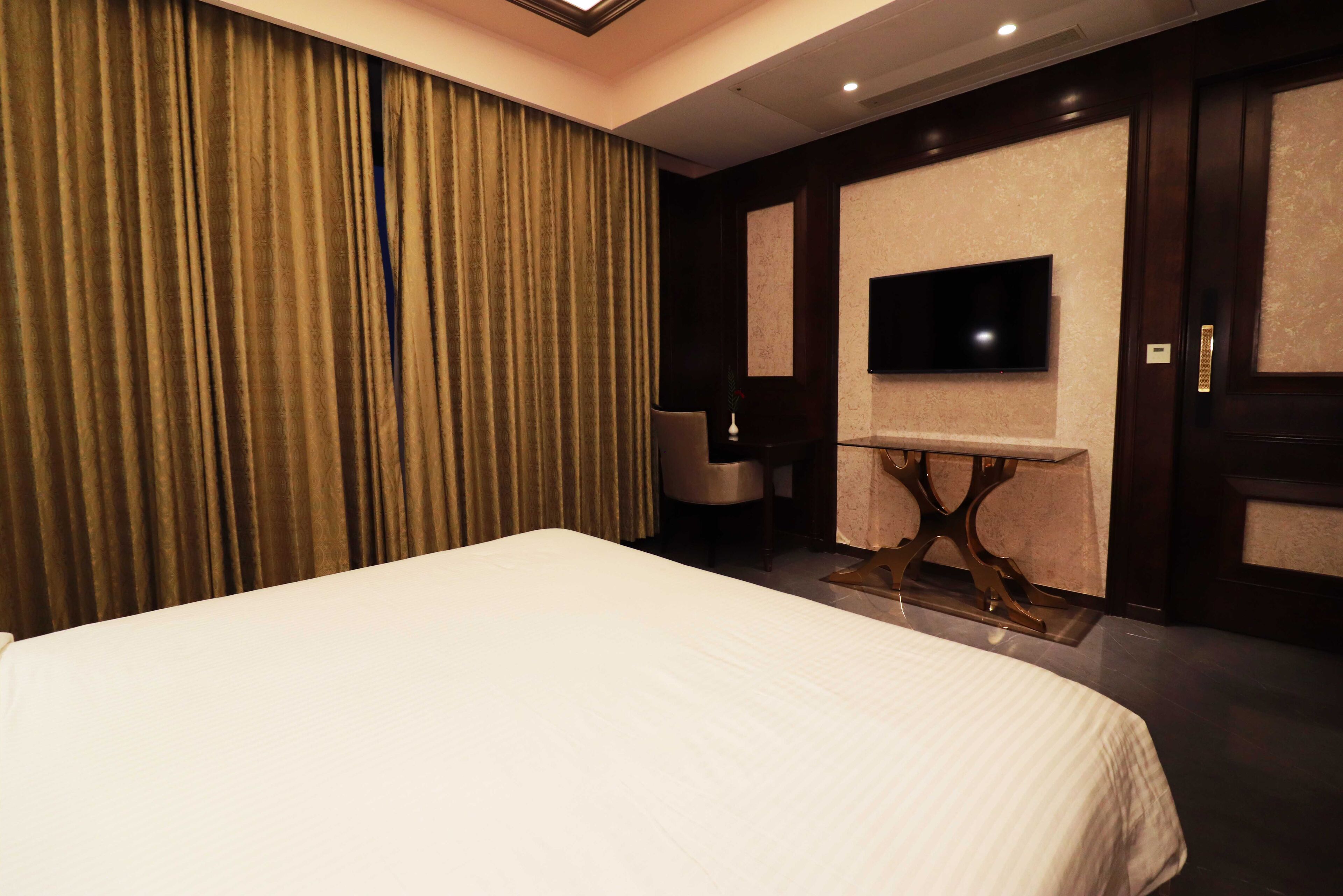Une chambre d’hôtel avec un grand lit, un téléviseur à écran plat fixé au mur, une petite table et une chaise.
