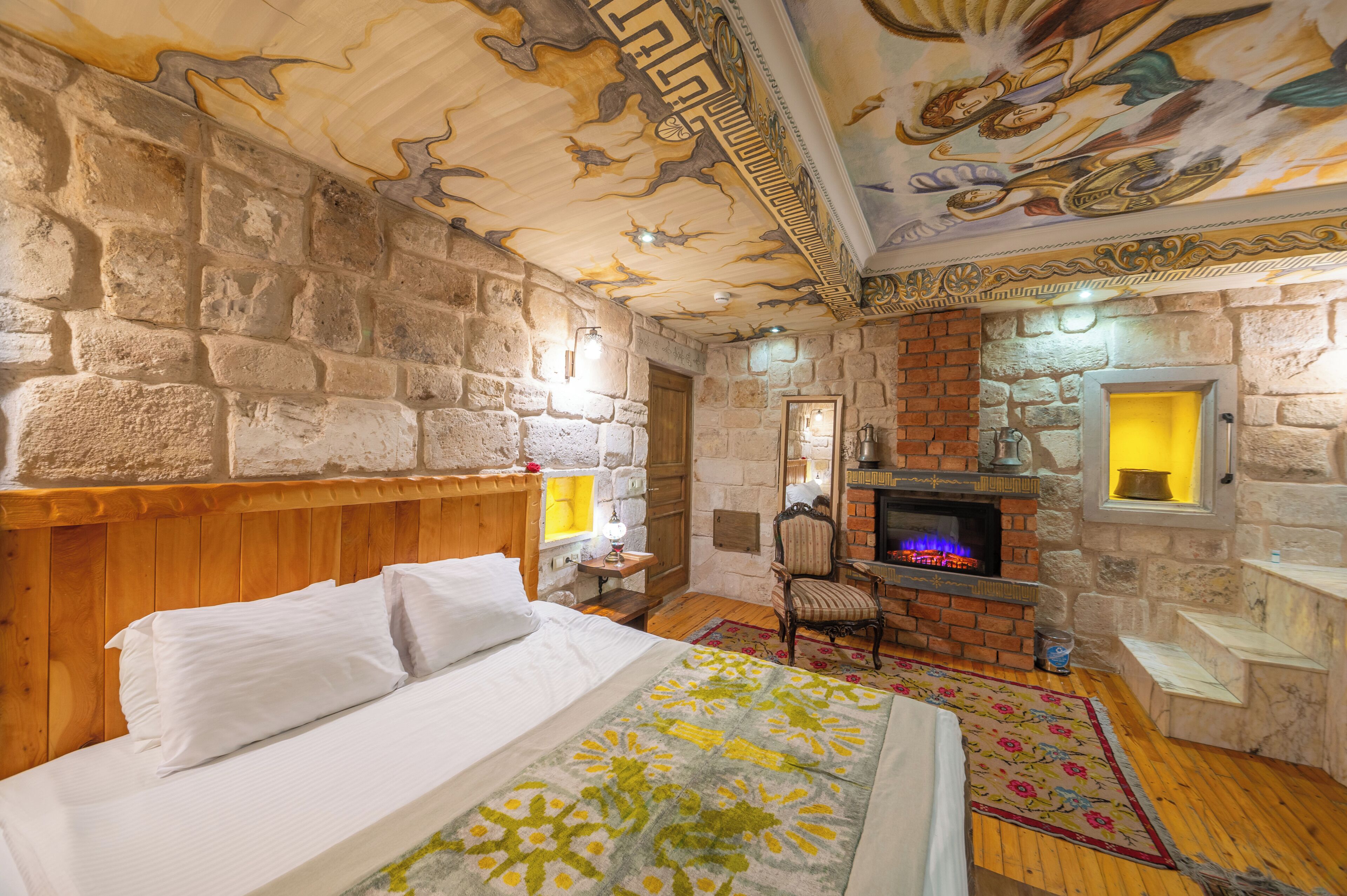 Une pièce avec un lit, une cheminée, des murs en pierre et une peinture murale au plafond.