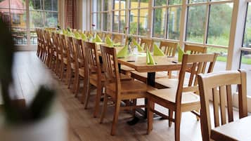 Une longue table à manger entourée de chaises, de grandes fenêtres et une vue sur la verdure environnante.