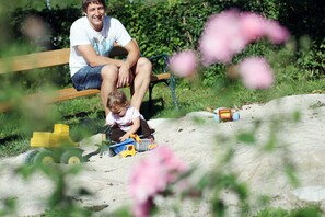 Eine Person sitzt auf einer Bank in einem Park mit Sand und Spielzeug.