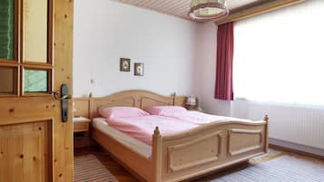 A bedroom with a wooden bed, a nightstand, a mirror, and a window with curtains.