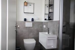 A modern bathroom with a toilet, sink, and shower. - Sonnengarten 3 - KüstenART (Kellenhusen)