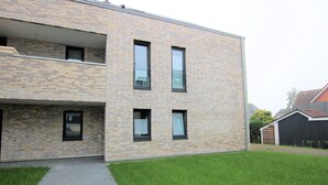 Un bâtiment moderne à deux étages, doté d’une façade en briques, de grandes fenêtres et d’un chemin pavé menant à une zone herbeuse.