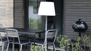 Un espace extérieur aménagé pour les repas, avec une table, des chaises, une lampe et un barbecue.