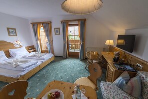 A hotel room with two beds, a wooden desk, a chair, a table with fruit, and a TV. - Gutshof Wolfgangsee Resort & Event Hotel (Strobl)