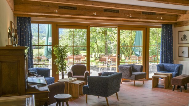 A spacious indoor area with wooden beams, large windows, and a variety of seating including armchairs and a piano. - Gutshof Wolfgangsee Resort & Event Hotel (Strobl)