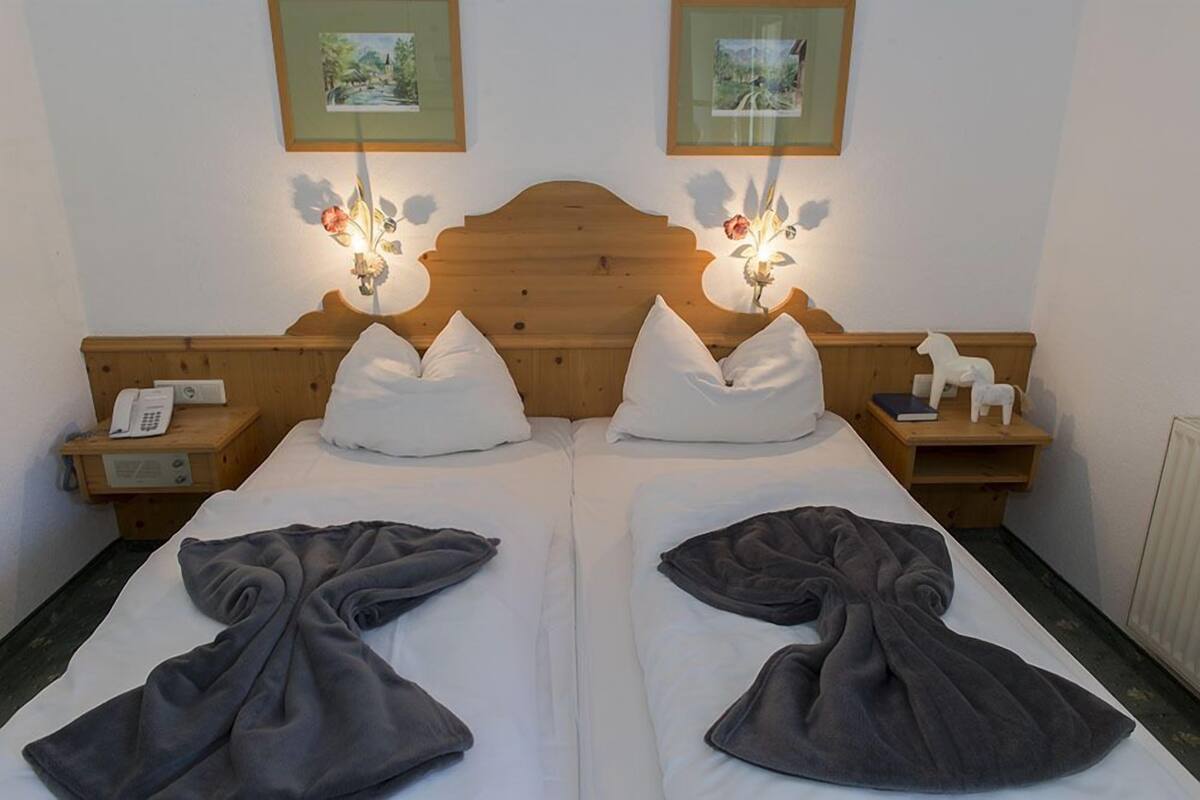 Un lit double avec du linge de lit blanc et deux peignoirs gris foncé. Il y a deux tables de chevet, l’une avec un téléphone et un livre, et l’autre avec une petite statue.