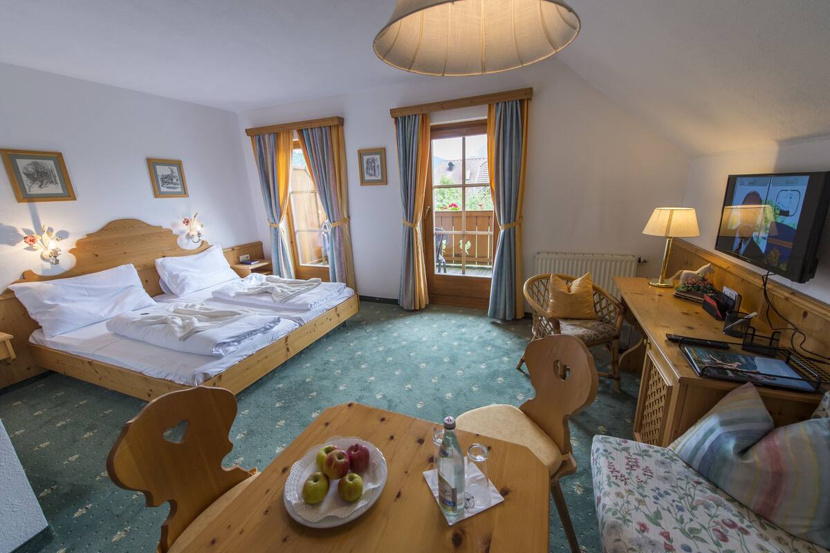 Une chambre d’hôtel avec un lit, un bureau, une chaise, une table avec des pommes et une bouteille, et un téléviseur.