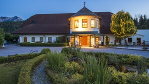 A traditional building with a round tower, a paved driveway, and a well-maintained garden. - Gutshof Wolfgangsee Resort & Event Hotel (Strobl)