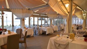A tented dining area with tables set for a meal, large windows, and a view of the outdoors. - Residence San Pellegrino (Penta-di-Casinca)