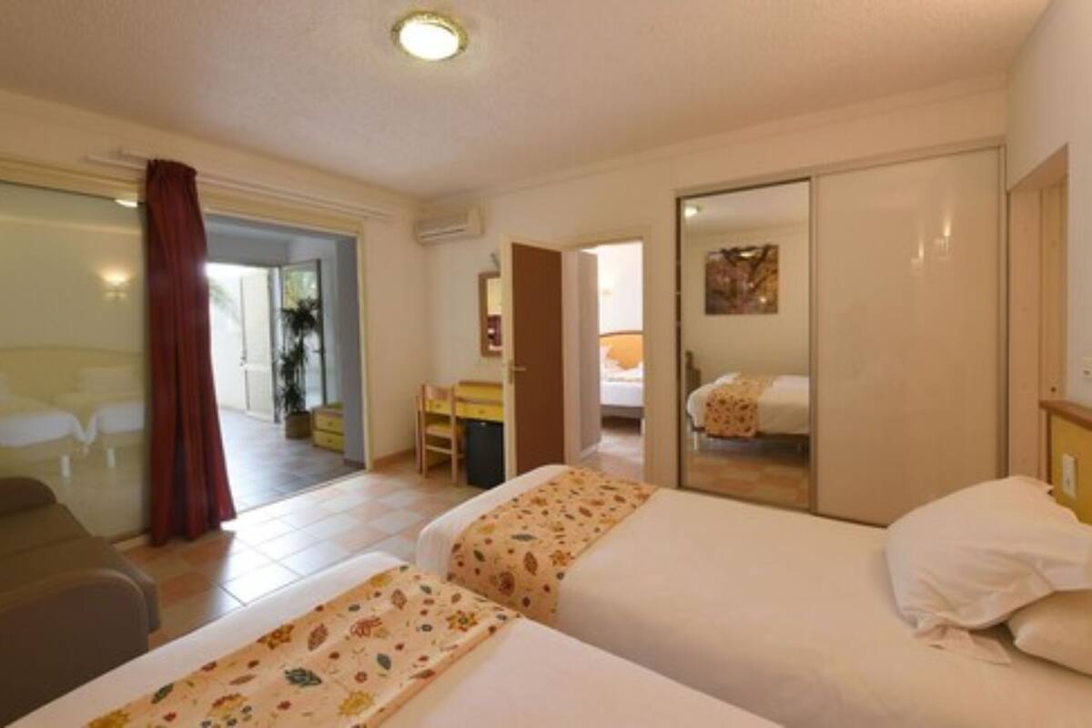 A hotel room with two beds, a sofa, a desk, and a bathroom.