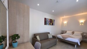 A modern hotel room with a sofa, a bed, a small table, and two potted plants. - Residence San Pellegrino (Penta-di-Casinca)