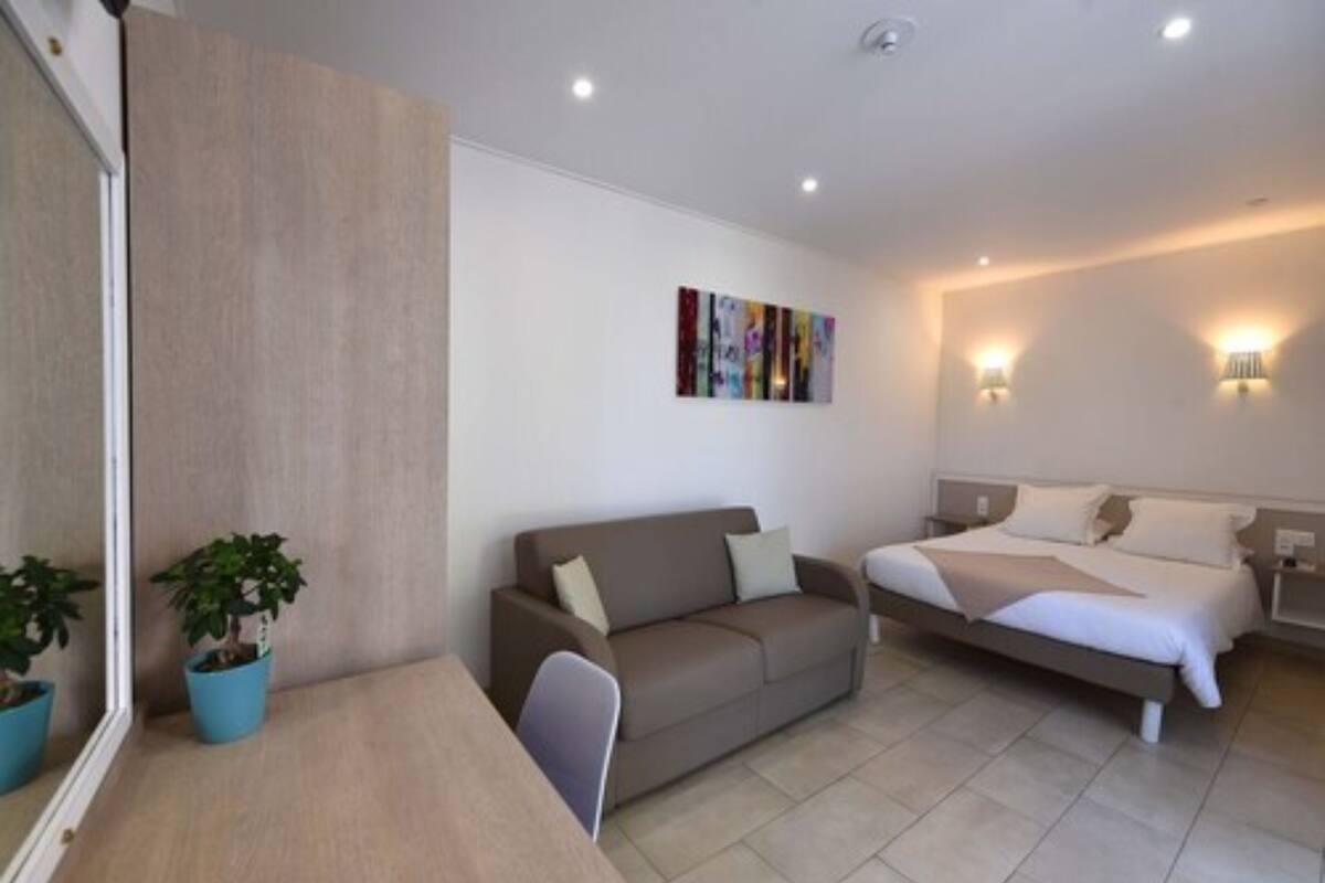 A modern hotel room with a sofa, a bed, a small table, and two potted plants.