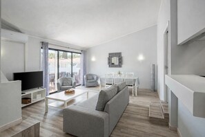Ein modernes Wohnzimmer mit grauem Sofa, einem Flachbildfernseher, einem Esstisch mit Stühlen und einem großen Fenster mit Vorhängen.