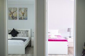 Une chambre à coucher avec un lit blanc, une table de chevet, une lampe et deux tableaux accrochés au mur.