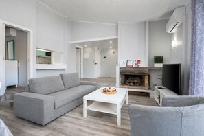 A modern living room with a grey sofa, a white coffee table, a fireplace, and a TV.