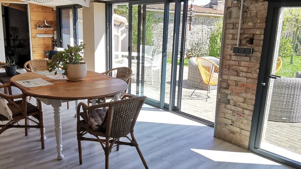 A dining area with a round wooden table, wicker chairs, and a potted plant.