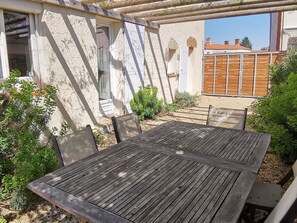 Una mesa de madera con sillas en un patio, rodeado de follaje y un muro de piedra.
