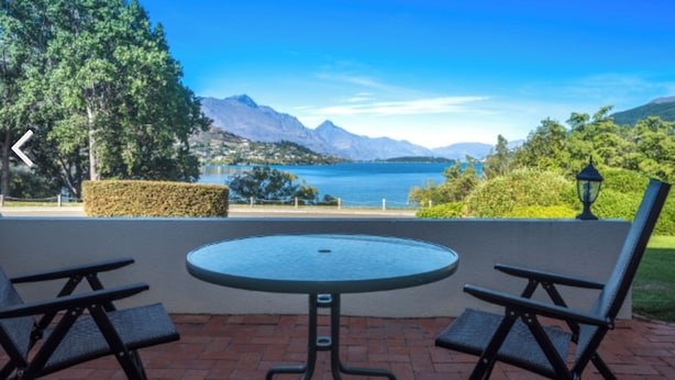 Een terras met een ronde tafel en twee stoelen, met uitzicht op een meer met bergen op de achtergrond.