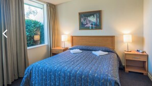 Hotelkamer met een groot bed, twee nachtkastjes, een raam met gordijnen en een schilderij aan de muur.