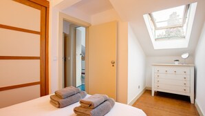 Un dormitorio con cama, cómoda, tragaluz y puerta que da a otra habitación.