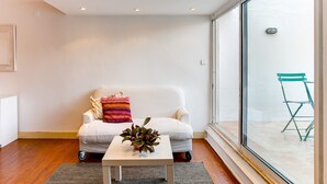 Una sala de estar moderna con un sofá blanco, una mesita pequeña con una planta y un ventanal con vistas al exterior.