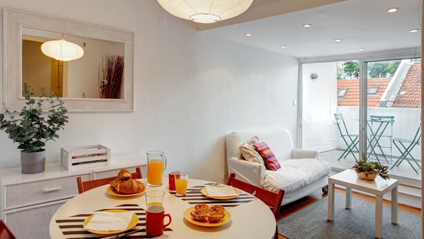 Una habitación moderna y luminosa con una mesa de comedor lista para el desayuno, un sofá y vistas al exterior.