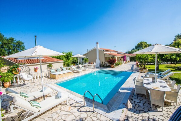 A swimming pool with lounge chairs and umbrellas, surrounded by stone tiles and potted plants.