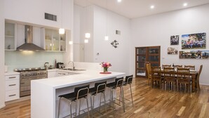 A modern kitchen with a central island, bar stools, a dining area with wooden chairs, and a large window. - Burnvale: spacious family home, 500m to beach, air-conditioned (Dunsborough)