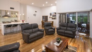 A modern living room with leather sofas, a wooden coffee table, and a dining area with wooden chairs. - Burnvale: spacious family home, 500m to beach, air-conditioned (Dunsborough)