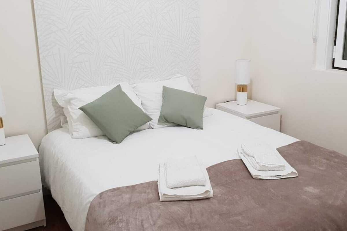 A neatly made bed with two pillows, a bedside table with a lamp, and a window.