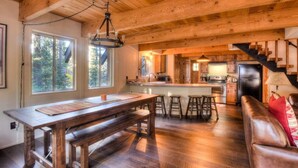 A rustic wooden interior with a dining table, bar stools, a leather couch, and a kitchen area with a refrigerator and wooden cabinets. - Enchanting Chamberlands Cabin (Tahoma)