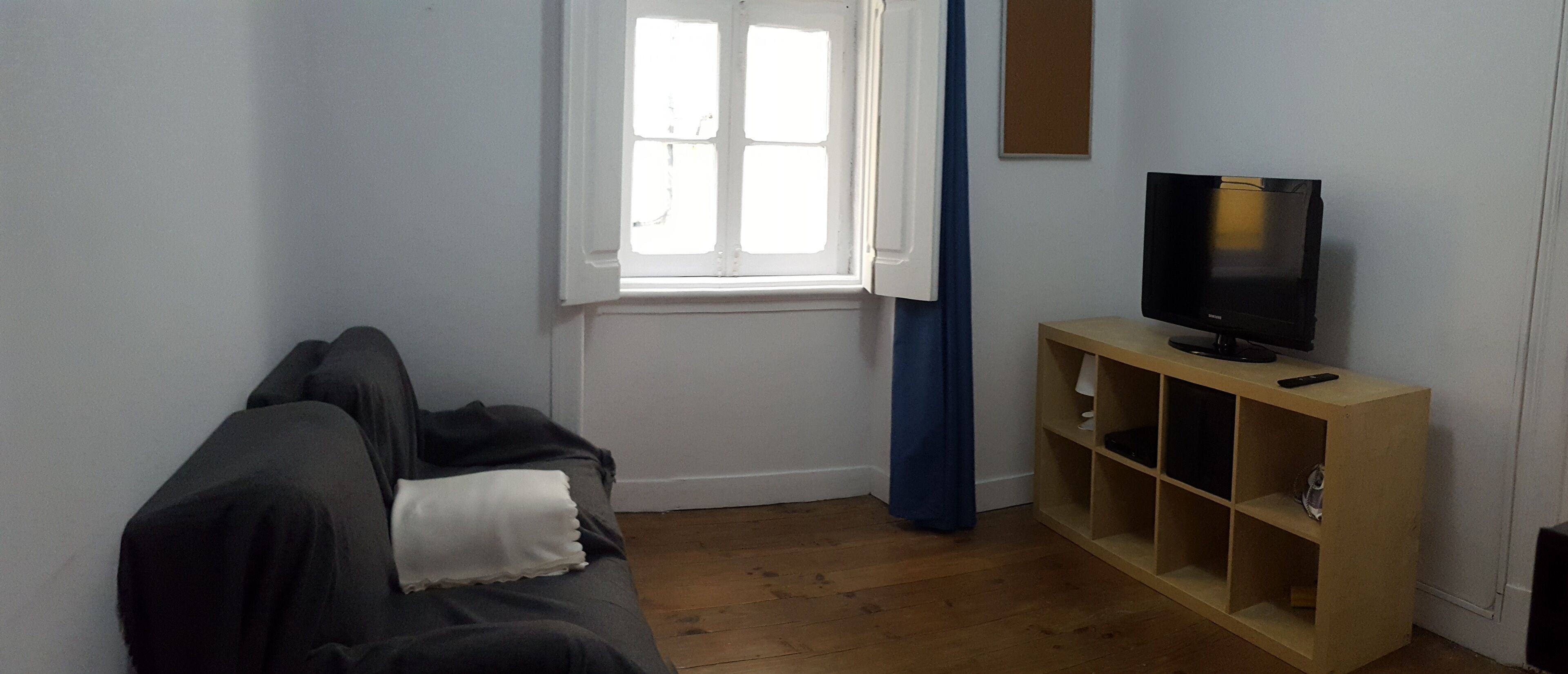 Una habitación con un sofá gris, un mueble bajo de televisión de madera y una ventana con cortinas.