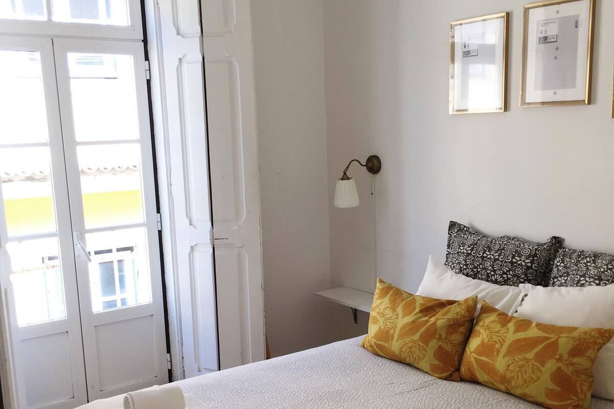 A bedroom with a bed, pillows, a bedside table, a lamp, and a door.