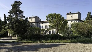 A two-story building with a symmetrical facade, surrounded by greenery and a gravel driveway.