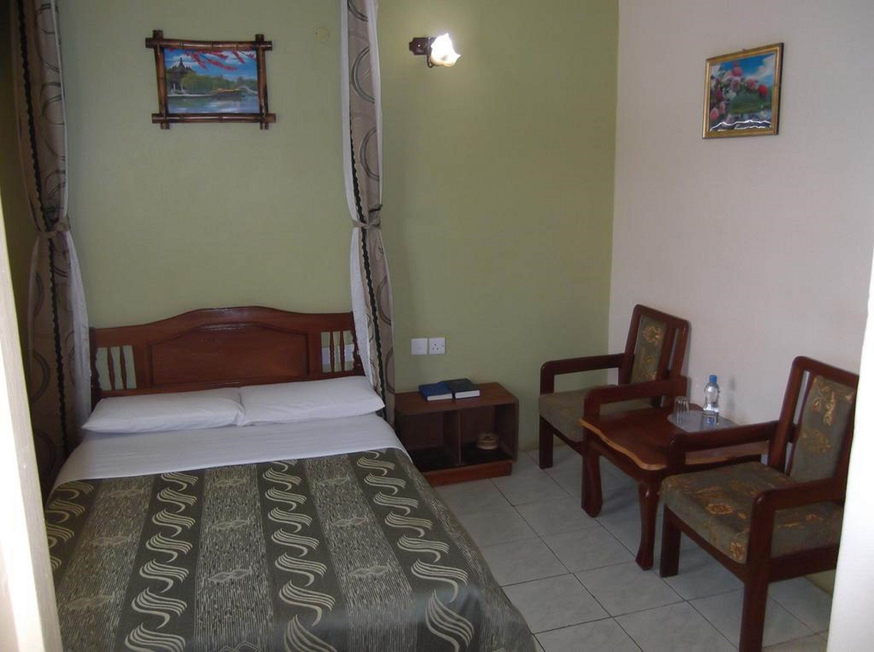 A room with a bed, a chair, a small table, and two paintings on the wall.