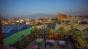 Un jardín en la azotea con plantas en macetas, mobiliario exterior y vistas a la ciudad y montañas al fondo.
