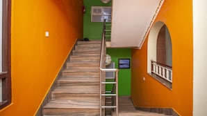 Una escalera con barandilla metálica que conduce a un rellano con pared verde y techo blanco.