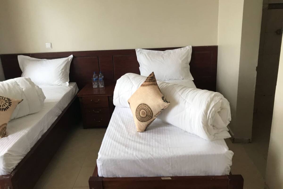 A hotel room with two beds, a wooden headboard, a nightstand with water bottles, and a pillow with a circular pattern.