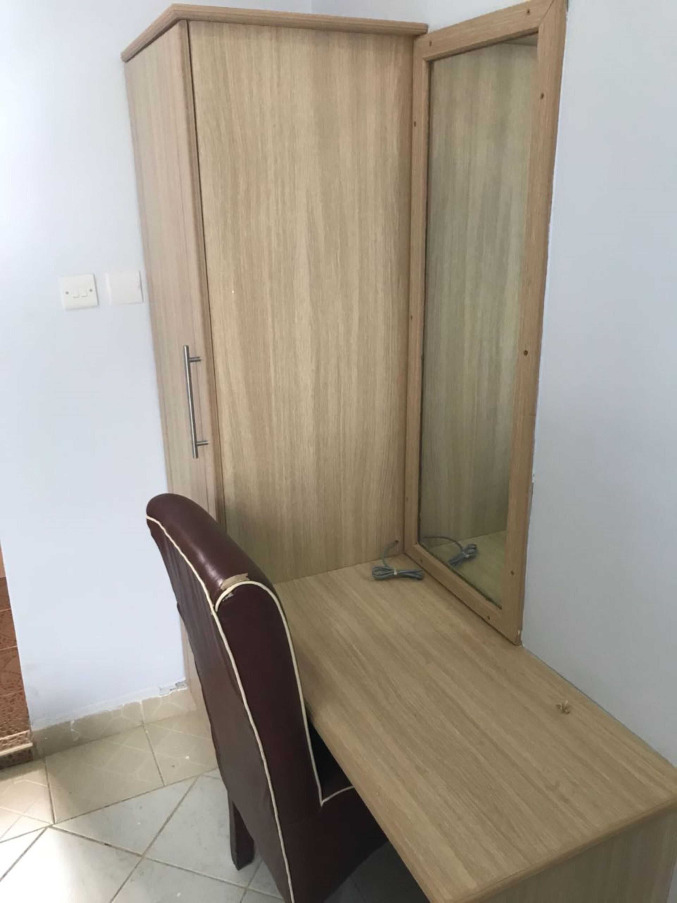 A corner room with a wooden wardrobe, a bench, and a mirror.