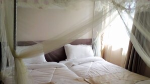 A bed with a canopy, white bedding, and a brown skirt. - Villa Rosa Mystica Hotel (Homa Bay)