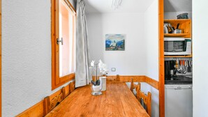 Une table à manger en bois avec des chaises, un tableau accroché au mur et un coin cuisine équipé d’un four à micro-ondes et d’ustensiles.