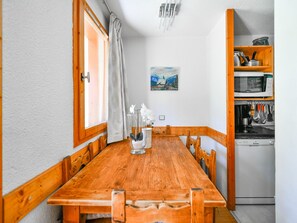 Une table à manger en bois avec des chaises, un tableau accroché au mur et un coin cuisine équipé d’un four à micro-ondes et d’ustensiles.